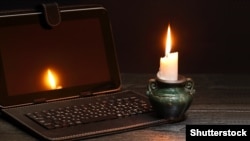 Blackout concept. Lighting candle near laptop with dark empty screen